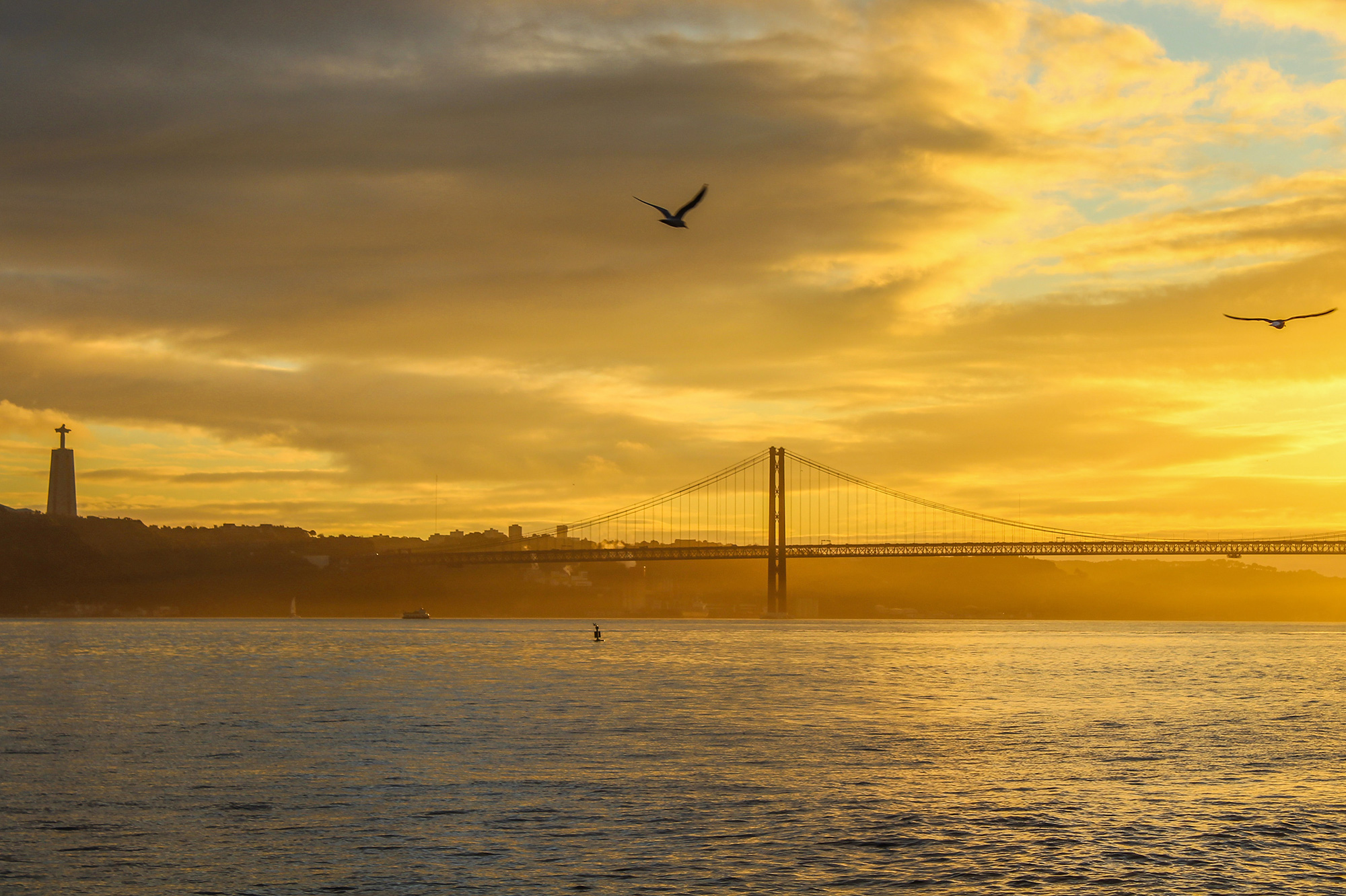 Sunset image of the Ponte 25 de Abril bridge in Lisbon Portugal with the Tagus river in the foreground