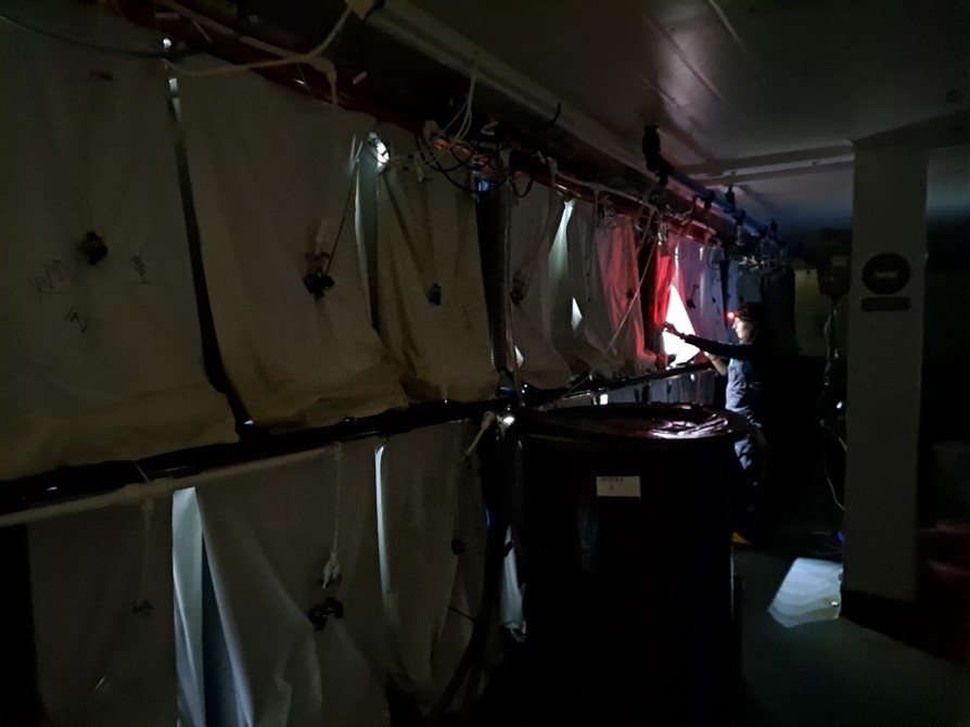 Dark room with separated pods with curtains across and one being opened by a scientist with a red headtorch
