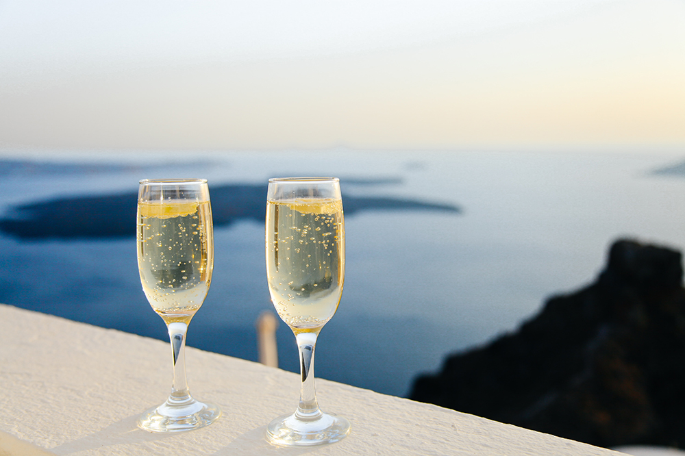 Two champagne glasses on a ledge overlooking the ocean in the background